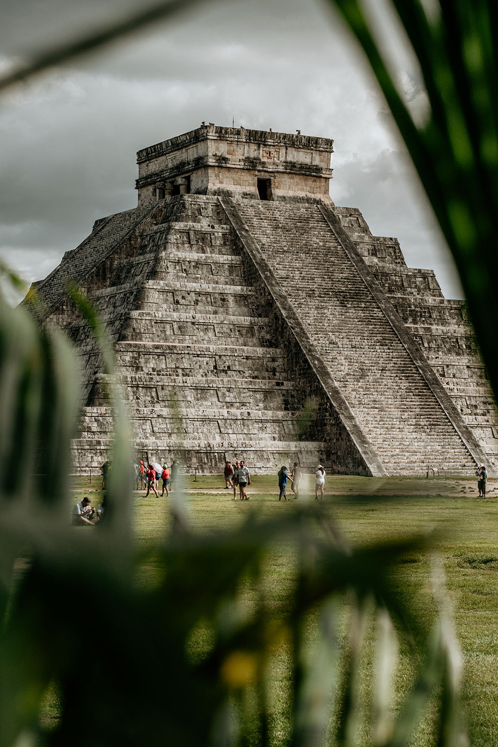 Pyramid of Chichén Itzá behind green leaves