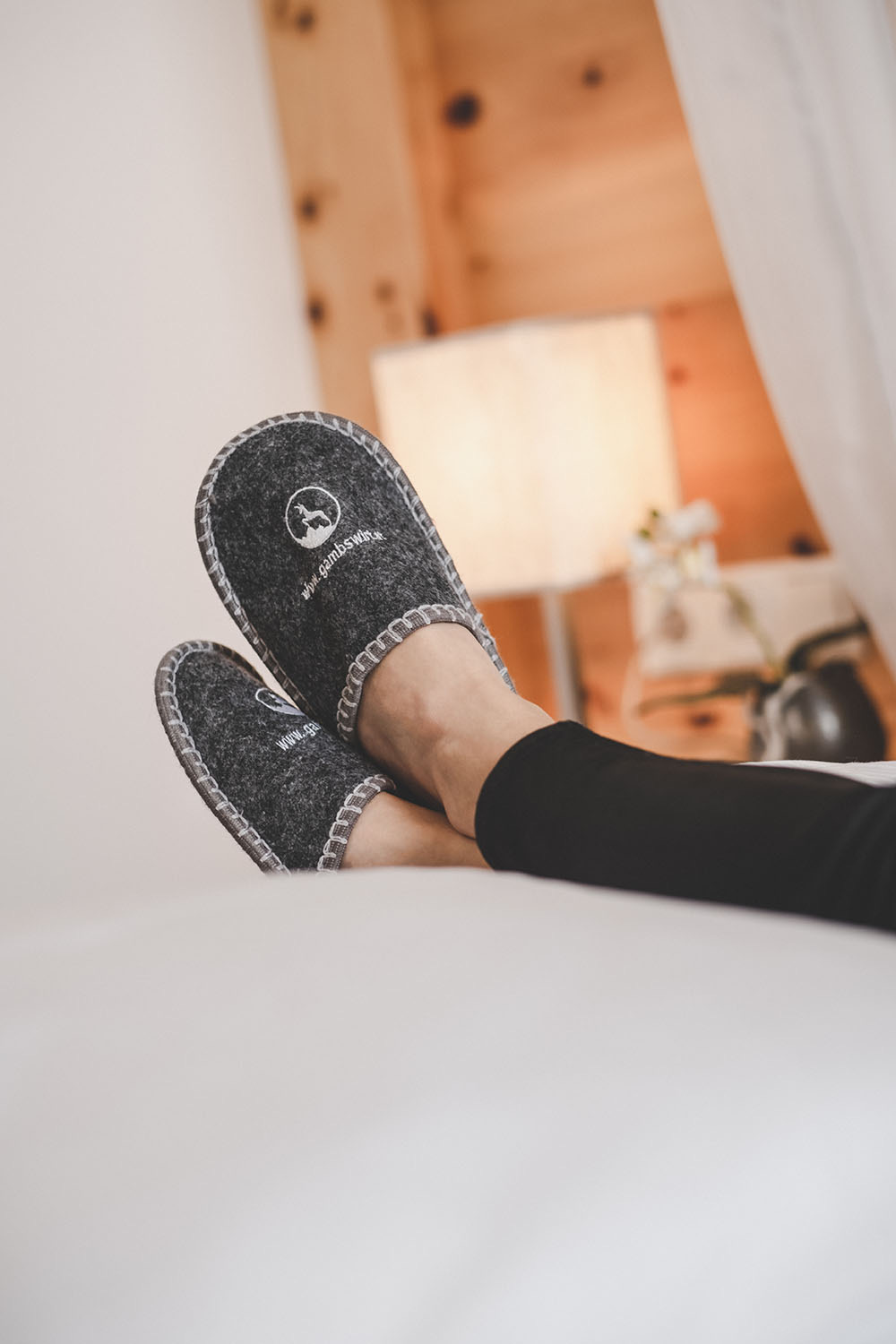 Feet in felt slippers on a bed in a wooden chalet