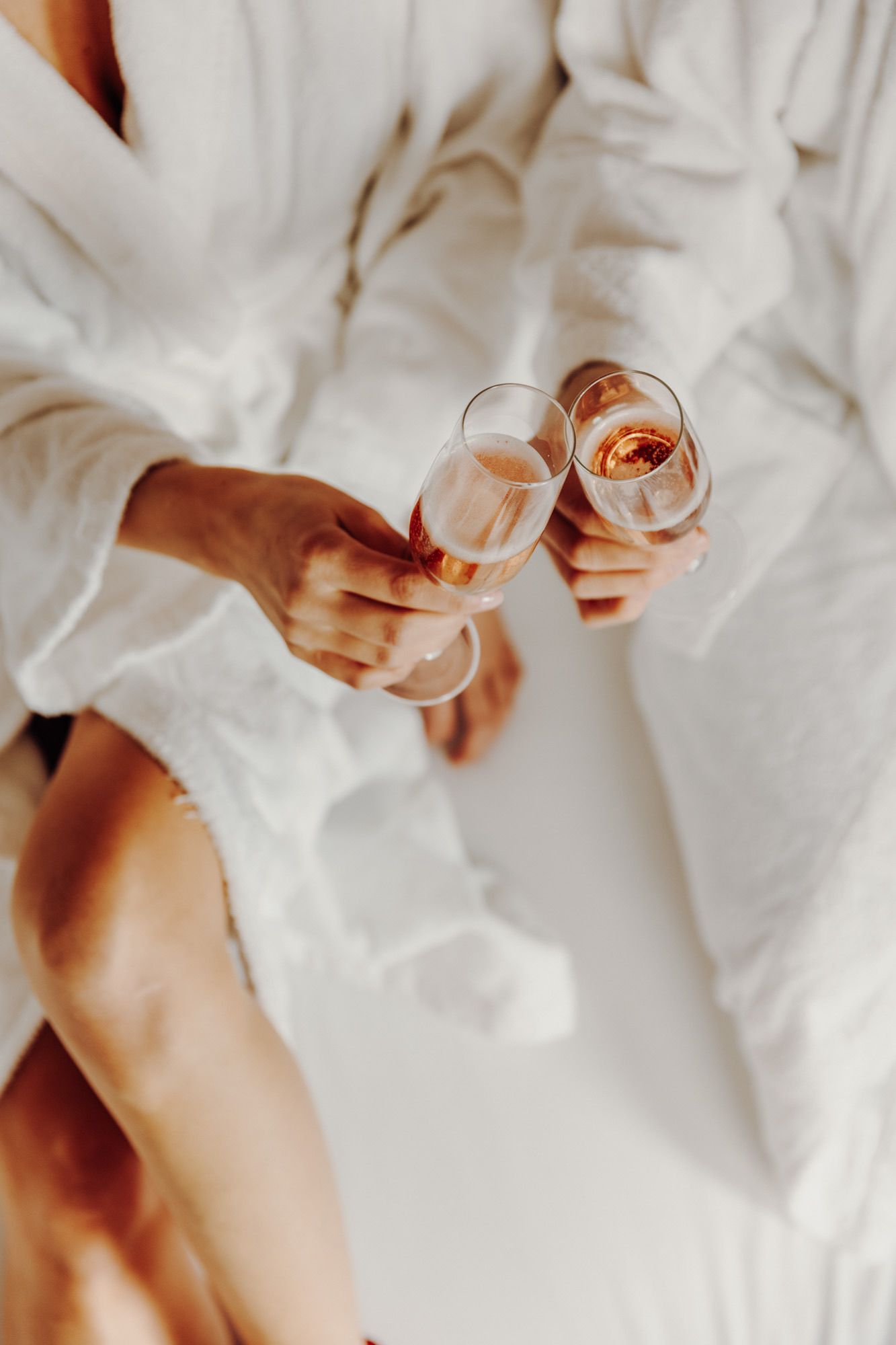 Two people in white bathrobes toasting with rosé